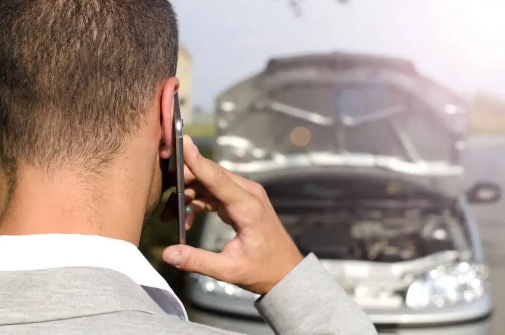 Man standing by broken vehicle calling tow service after traffic accident
